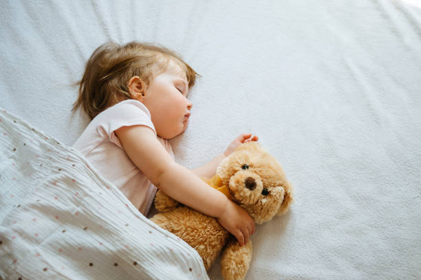 A baby sleeps beside her teddy bear.
