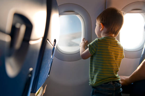 Young child in a green striped shirt standing and looking out of an airplane window during flight