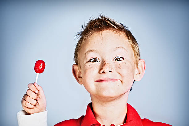A smiling boy holding a red lollipop