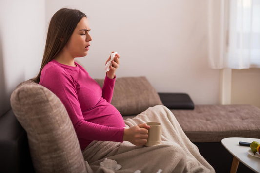 Pregnant woman sitting on a couch, holding a mug and tissue