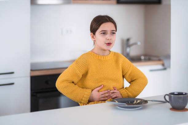 Young girl in a yellow sweater holding her stomach and appearing to be in discomfort