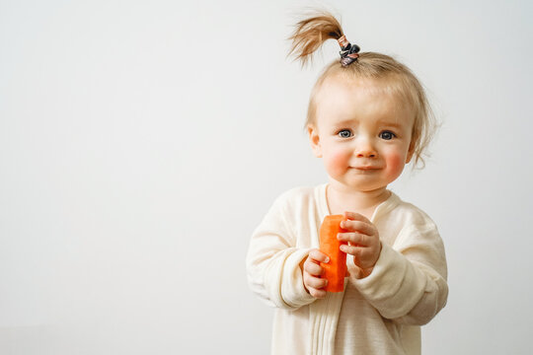 A baby holding a carrot suffers from a food allergy.