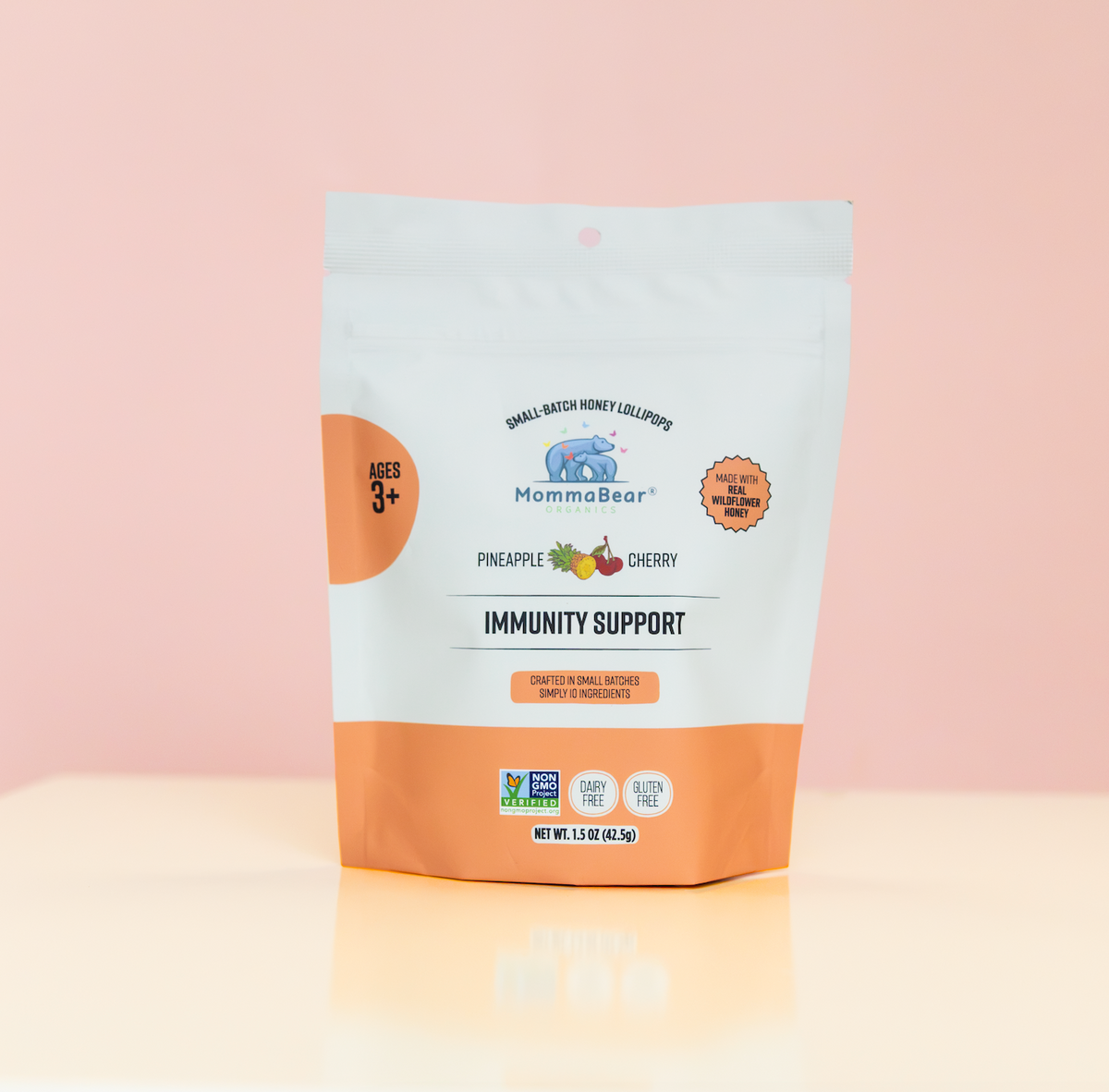 A stand-up pouch of MommaBear Small Batch Honey lollipops Immunity Support  in Pineapple & cherry flavor. The packaging is white with a peach-orange bottom section 